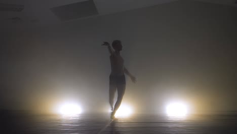 slow shutter effect of moving modern male dancer in dark studio with backlights and dense smoke