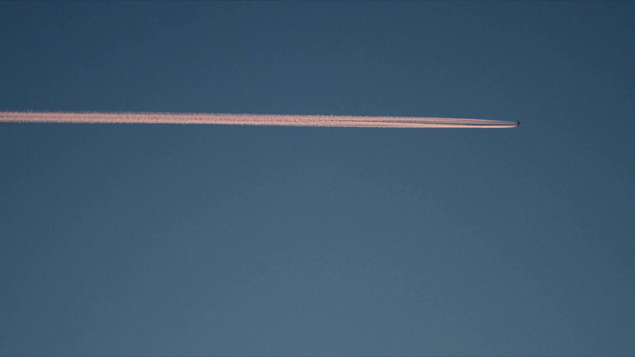 Jejak kondensasi pesawat yang panjang melintasi langit Arktik biru lembut di atas hutan belantara Norwegia