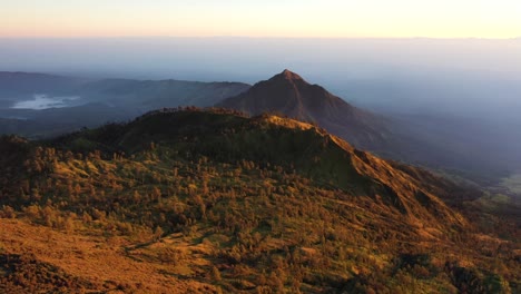 Atemberaubende-Luftaufnahme-Einer-Wunderschönen-Bergkette,-Die-Bei-Sonnenaufgang-Von-Wolken-Umgeben-Ist