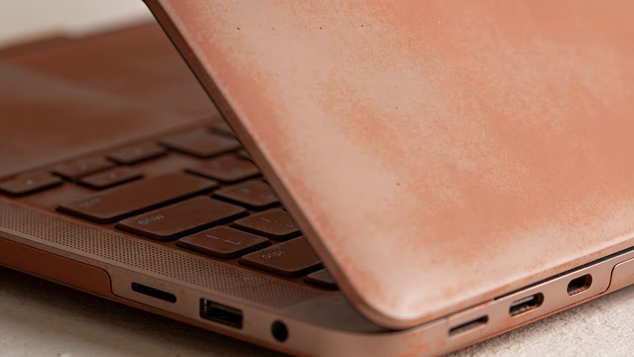 Chiusura di un laptop color oro rosa, con il coperchio che si abbassa tramite la cerniera su una superficie morbida, a protezione della tastiera chiclet.