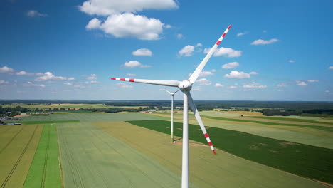 large spinning wind turbine situated in the middle green field, surrounded by a patchwork of farmland, windmill blades turning generating clean energy - aerial close-up