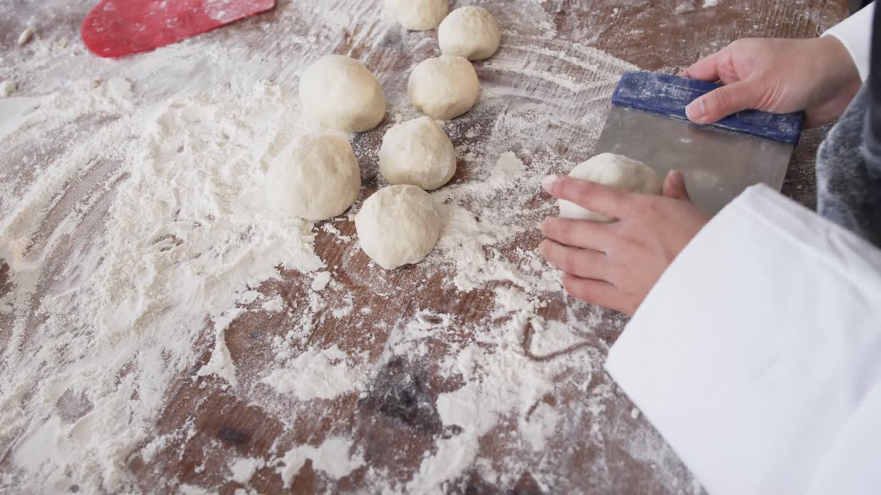 Asian female baker working in bakery kitchen, making rolls from dough in slow motion