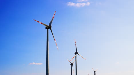 rotating blades of wind turbines at the backdrop of blue clear sky. green energy production concept. low angle view.