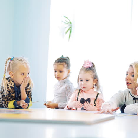 children with their teacher together at round table in class. little kids studying english while playing with pictures at elementary school.