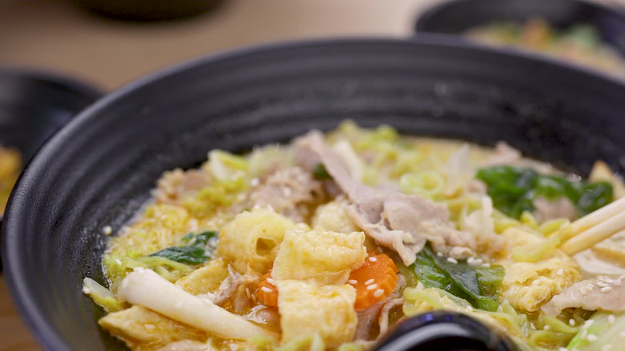Close-up of chopsticks lifting green noodles from vibrant Asian soup in warm indoor lighting