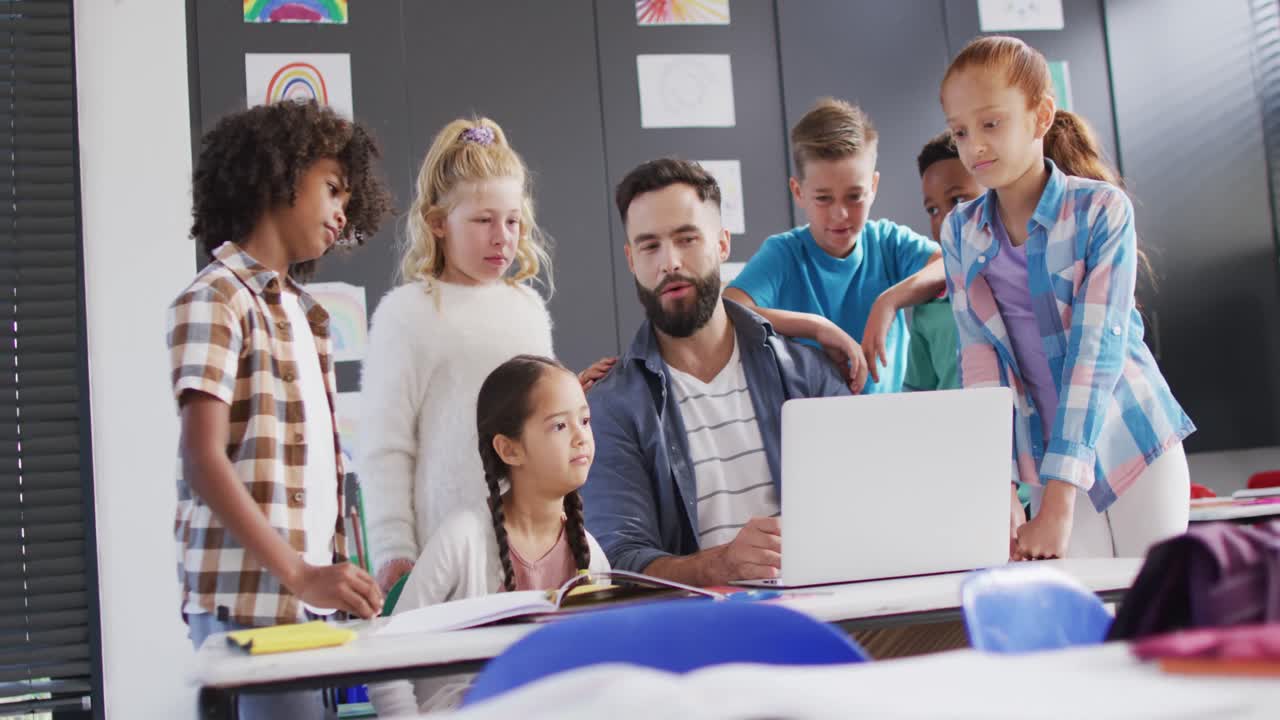 Diverse male teacher and happy schoolchildren using laptop in school classroom