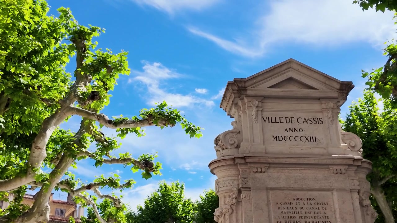 Inquadratura dal basso di un monumento in pietra provenzale incorniciato da alberi verdi e nuvole.