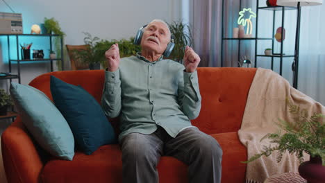happy grandfather old man in wireless headphones relaxing on sofa at home listening favorite music