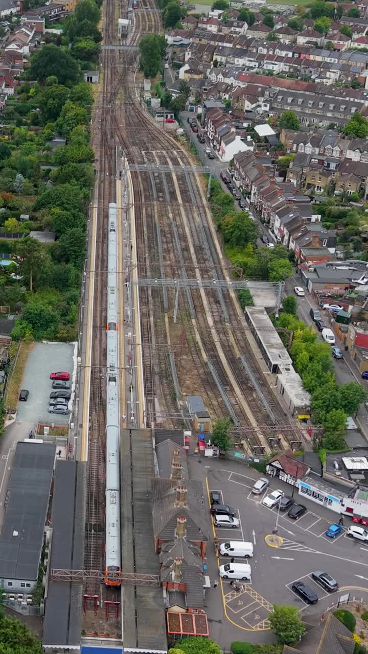 Vertical forward drone flight over Chingford bus station toward railway terminus, where one train sits in the station and the other seven lines remain empty, showing London’s transport hub from above