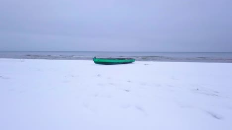 Luftaufnahme-Der-Ostseeküste-An-Einem-Bewölkten-Wintertag-Mit-Grünem-Küstenfischerboot,-Strand-Mit-Weißem-Sand,-Der-Von-Schnee-Bedeckt-Ist,-Küstenerosion,-Weitwinkeldrohnenaufnahme,-Die-Sich-Tief-Vorwärts-Bewegt