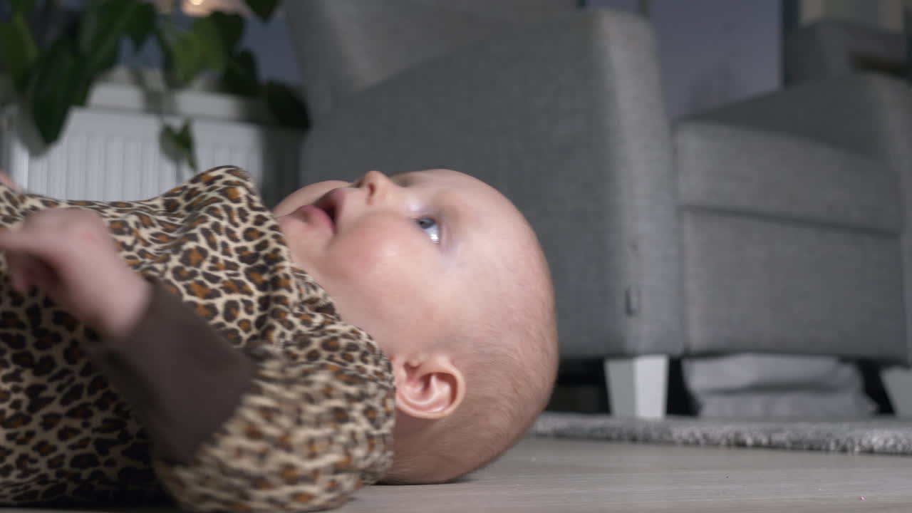 그녀가 일어날 수 없기 때문에 바닥에 구르는 점박이 onesie에 파란 눈의 어린 소녀의 클로즈업과 긴장