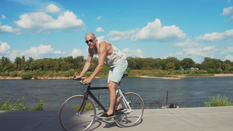 relaxed man riding bicycle along city riverside. profile view