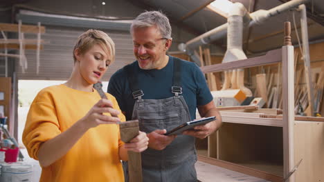 aprendiz femenina aprendiendo de un carpintero adulto con una tableta digital en un taller de muebles