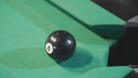 close-up of black billiard ball rolling toward pool pocket after being struck by white cue ball on green felt table. focus on precision, motion of gameplay with dramatic lighting and shadows