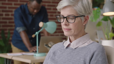 Una-Mujer-De-Negocios-Madura-Se-Pone-Gafas-Y-Parece-Una-Lectura-Relajada-En-Un-Espacio-De-Trabajo-De-Oficina-Moderno-Disfrutando-De-Un-Hito-Profesional-Exitoso