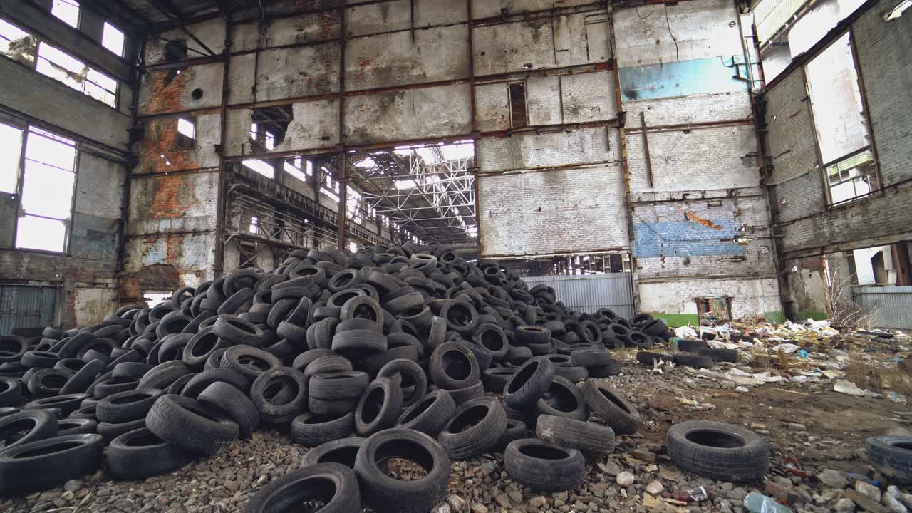 Many waste rubber tires lying on the ground inside the old factory. Big pile of used black car wheels on the empty territory. Camera moves bottom up