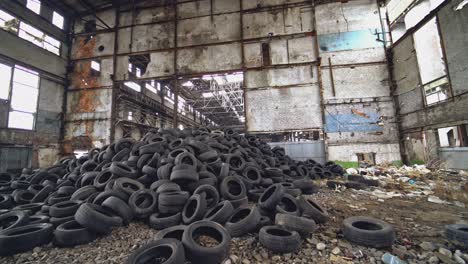 many waste rubber tires lying on the ground inside the old factory. big pile of used black car wheels on the empty territory. camera moves bottom up