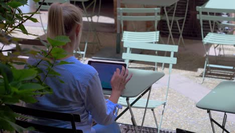 A-blonde-Caucasian-woman-sitting-on-a-terrace-using-her-smartphone-and-tablet-while-surfing-the-internet
