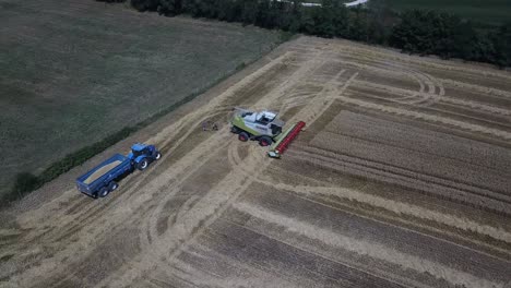 A-cinematic-4K-drone-shot-of-a-combine-harvester-and-a-tractor-harvesting-a-field-in-France,-showcasing-agriculture