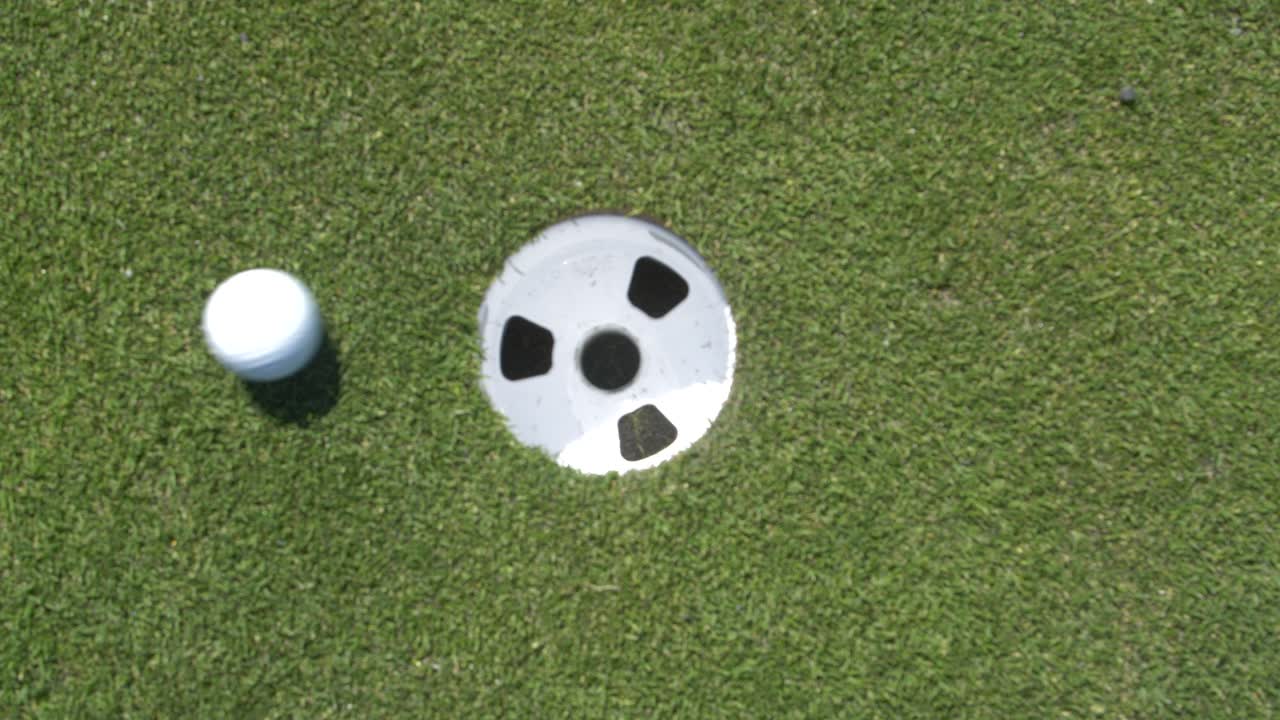 pelota de golf entrando en el hoyo con putter profesional en green