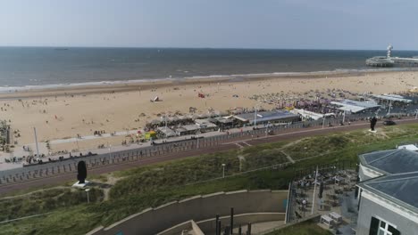 Cámara-Lenta-De-Drones-De-La-Playa-De-Scheveningen-Con-El-Muelle-Al-Fondo-Durante-El-Clima-Cálido