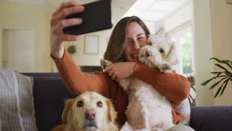 Mujer-Caucásica-Sonriente-Tomándose-Selfie-Con-Un-Teléfono-Inteligente-Y-Acariciando-A-Su-Perro-Mascota-En-Casa