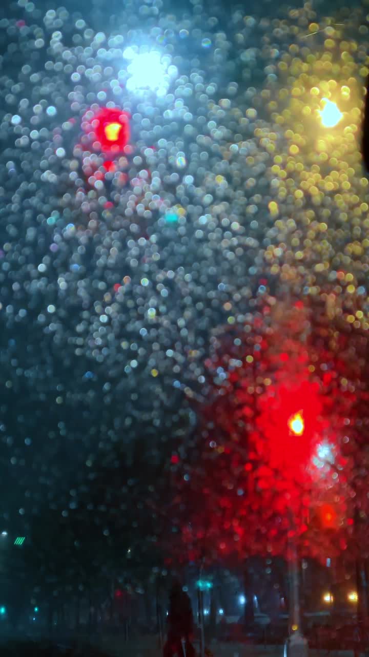 Rain drops and traffic lights through window. Out of focus rain drops on glass with red, yellow and white traffic lights at night