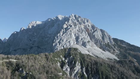 drone view of mangart mountains, slovenia: jagged peaks, rugged cliffs, lush green valleys, winding alpine roads, dramatic landscape, clear skies, julian alps, untouched natural beauty