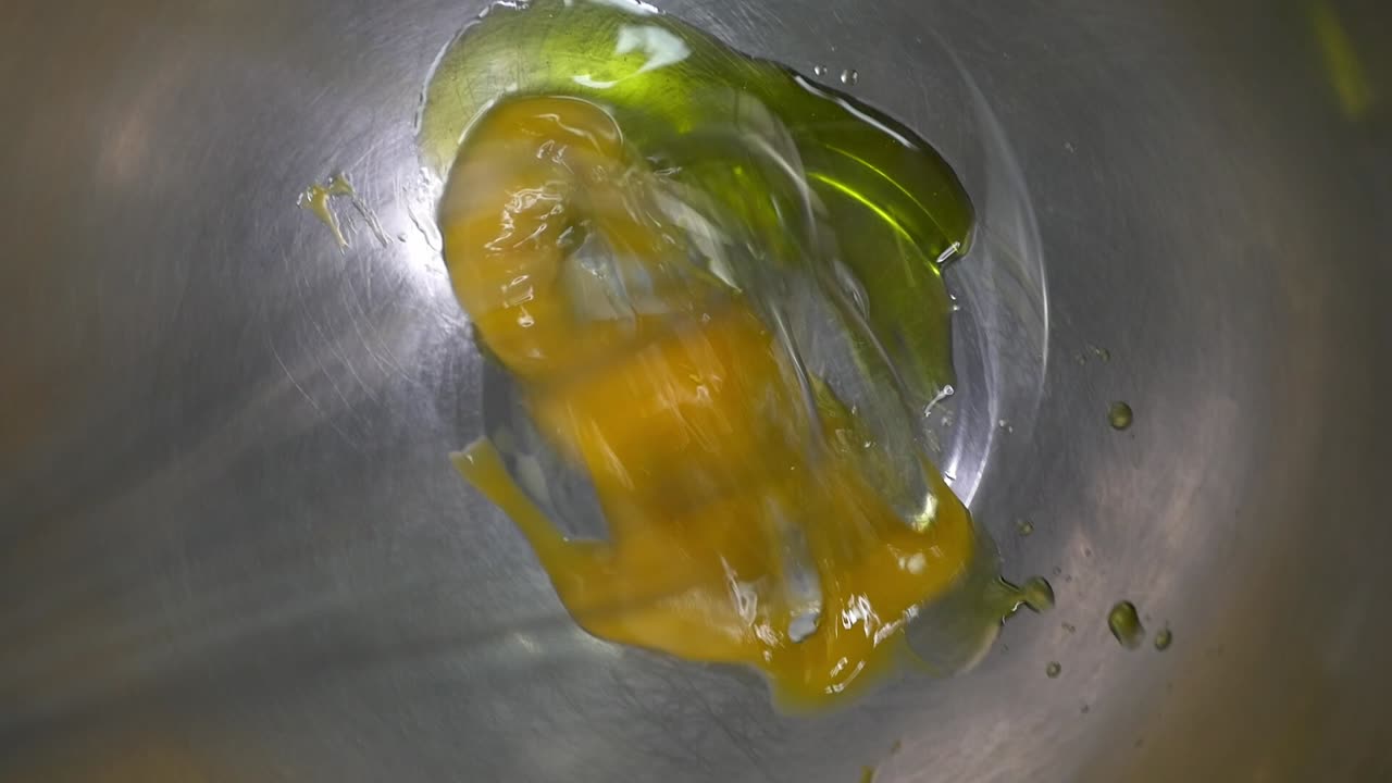 Preparing a sauce or dressing. A cook vigorously whisks fresh egg yolk with virgin olive oil in a steel bowl to create an emulsion