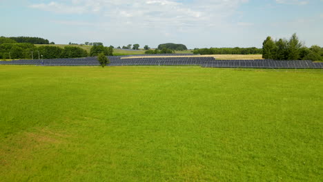 aerial fly over solar farm built in the middle of a green grassy field in zielenica, poland on summer day, template copy space