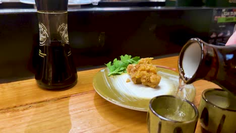 sake being poured alongside chicken karaage dish