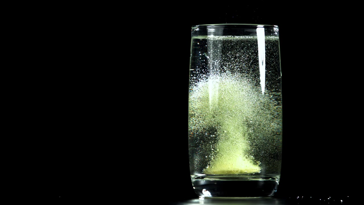 黒い背景のグラスの水に溶ける発泡錠