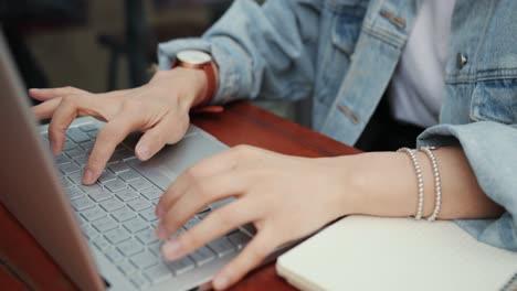 close up of the female hands tapping and texting on the keyboard of laptop computer on the table in the cafe outside terrace