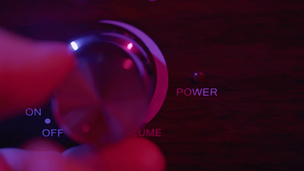Hand Adjusting Volume Knob on Audio Amplifier in Dark Room