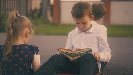 little girl with pencil talks to boy reading book on street