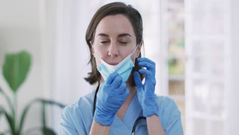 Portrait-of-caucasian-female-doctor-wearing-face-mask-at-home