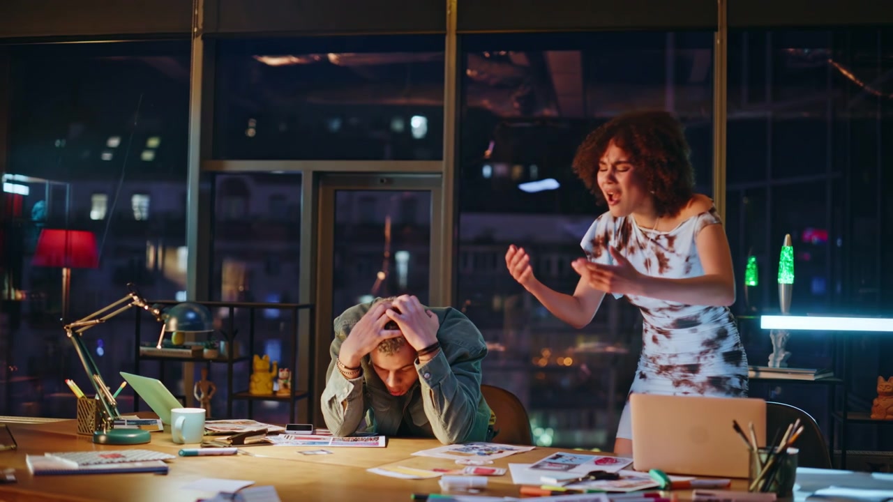 Coworkers reacting to phone news office night. Man and woman shocked at bad news