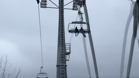 Cable-car-ski-lift-station-at-the-end-of-winter-with-some-skiers-and-snoboard-riders-with-massive-pillar-between-winter-forest