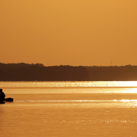 old fisherman in a boat on orange background of sunset. beautiful evening river and a man floating in a rowboat with fishing rods.