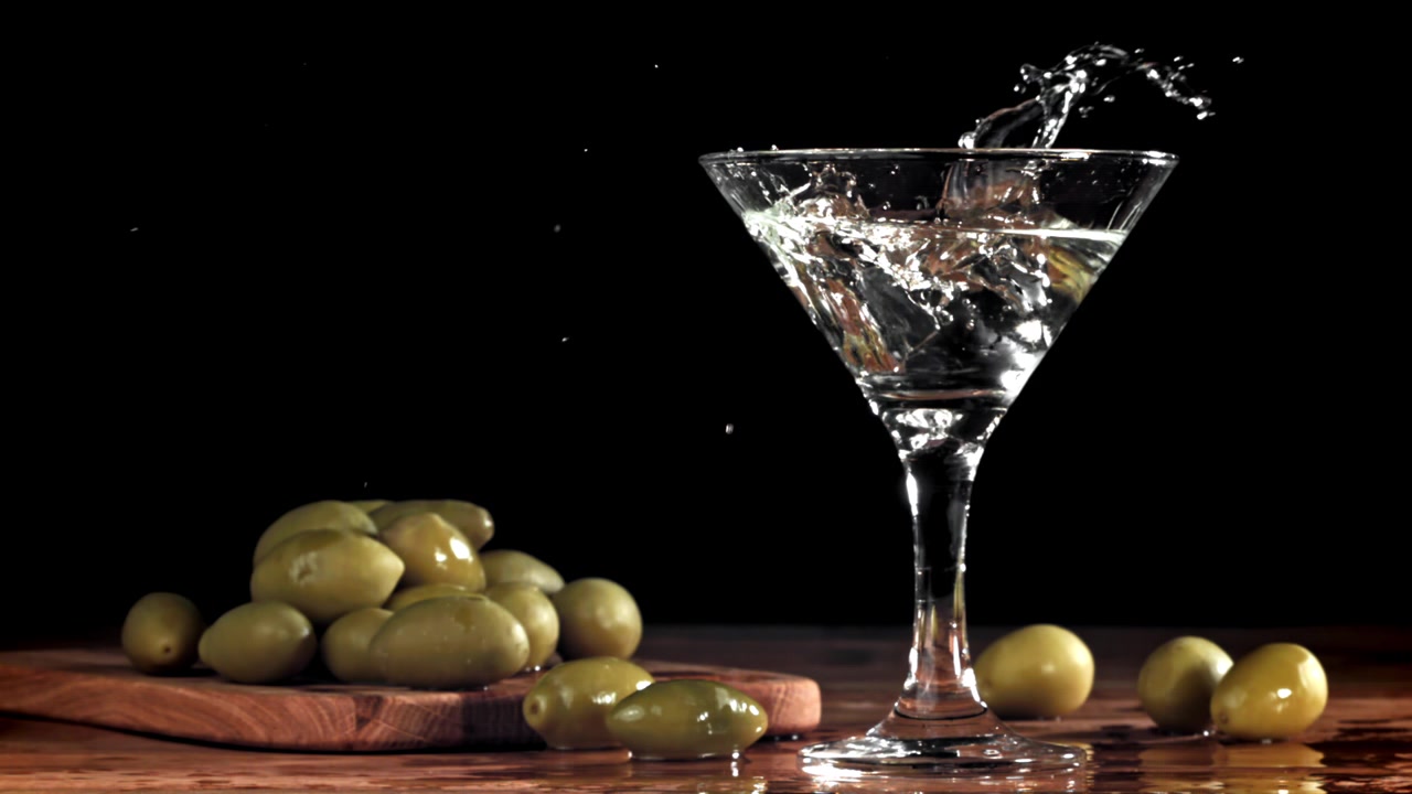 Schizzo di cubetto di ghiaccio al rallentatore in un bicchiere da Martini con olive.