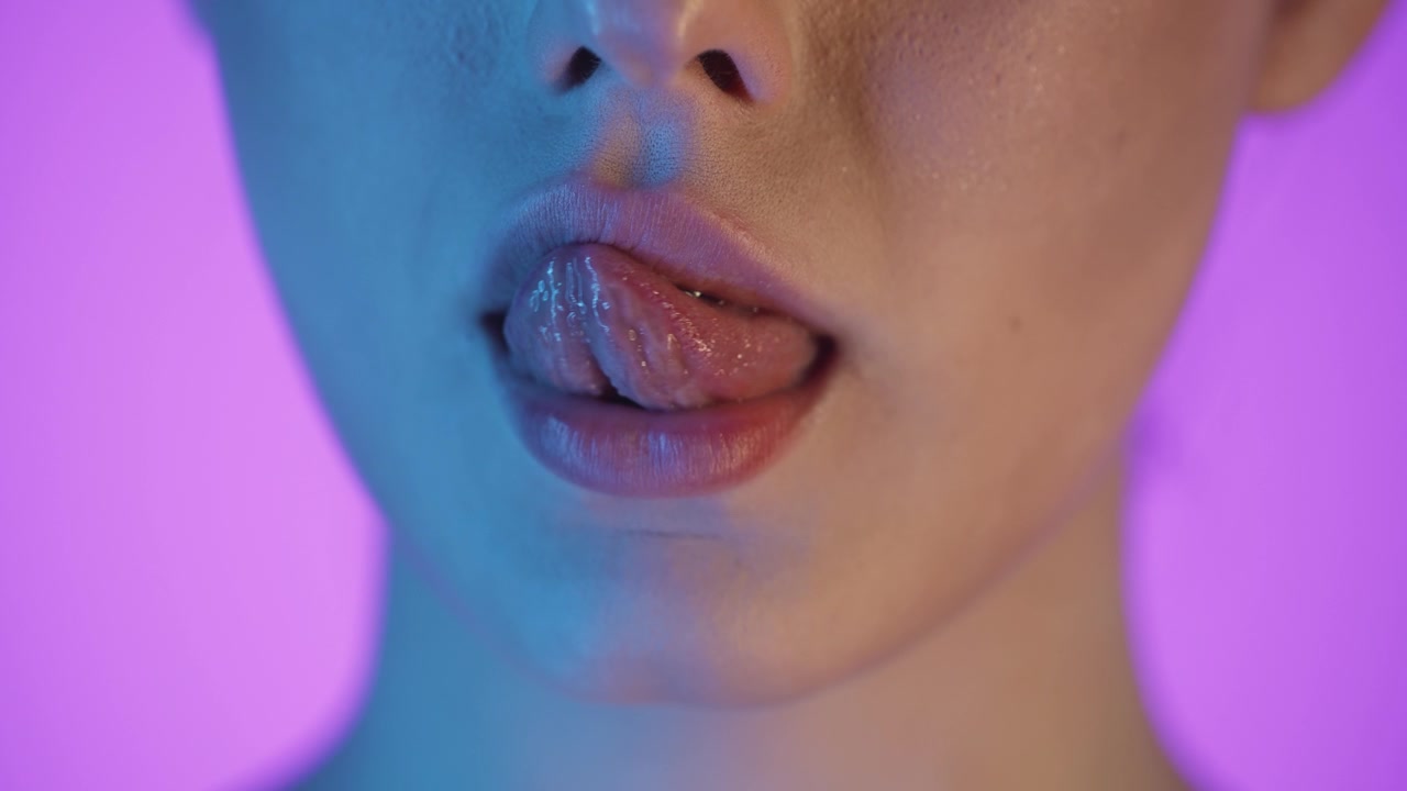 Primo piano della bocca di una donna che si lecca le labbra con la lingua, scatto in studio colorato