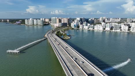 aerial view of sarasota, florida, showing a scenic coastal bridge, waterfront buildings and a boat speeding through clear blue water on a sunny day. wide shot.