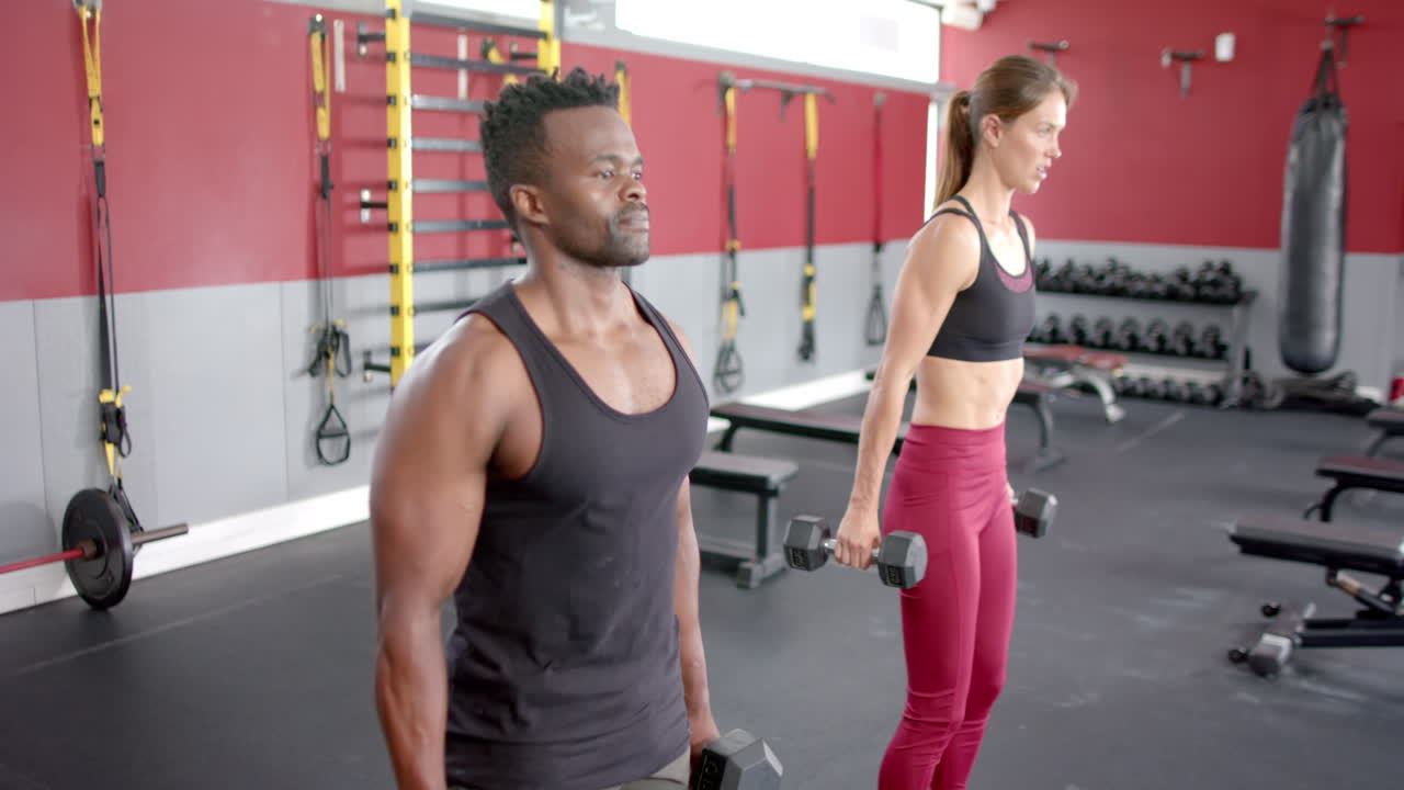 Afroamerikanischer Mann und junge kaukasische Frau stemmen Gewichte im Fitnessstudio
