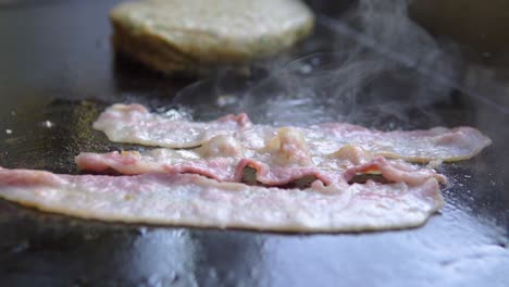 Cocinando-Rebanadas-De-Tocino-En-Una-Parrilla-Junto-A-Una-Hamburguesa-En-Un-Restaurante-De-Comida-Rápida-A-Cámara-Lenta