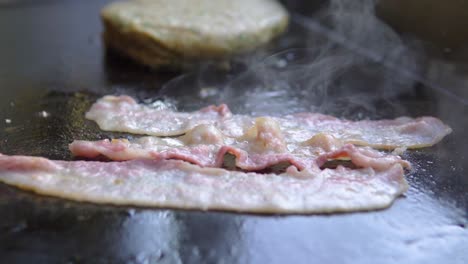 cocinando rebanadas de tocino en una parrilla junto a una hamburguesa en un restaurante de comida rápida a cámara lenta