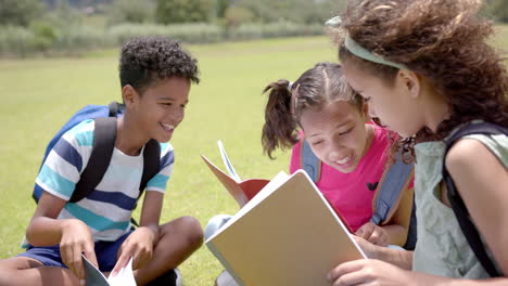 biracial children, a boy and two girls, read a book outdoors at school