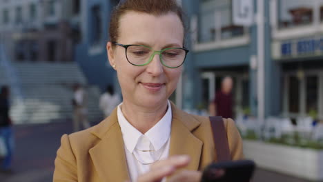 Primer-Plano-Retrato-De-Una-Elegante-Mujer-De-Negocios-Madura-Sonriendo-Revisando-Mensajes-En-Redes-De-Mensajes-De-Texto-De-Teléfonos-Inteligentes-Usando-Chaqueta-De-Traje-En-La-Ciudad