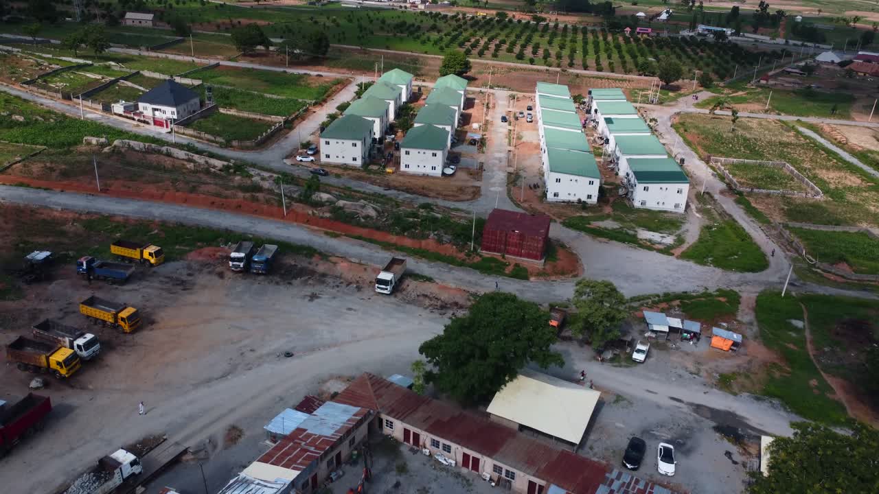 Aerial of housing development with red roofs and road grid near outskirts of Abuja, Nigeria, juxtaposed to sheet metal construction site. Newly built Isolated green roof estate in countryside Africa