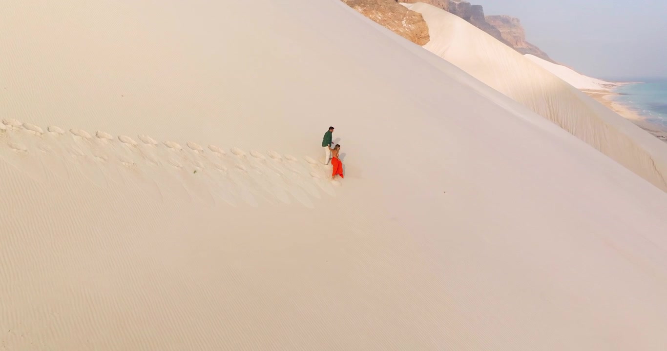Coppia che si tiene per mano corre giù per il pendio di una duna di sabbia bianca lasciando impronte sulla duna di sabbia di Arher nell'isola di Socotra, Yemen. - ripresa aerea