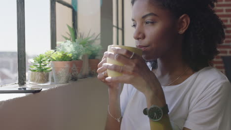 beautiful african american woman drinking coffee at home using smartphone enjoying relaxed morning browsing messages looking out window texting on mobile phone